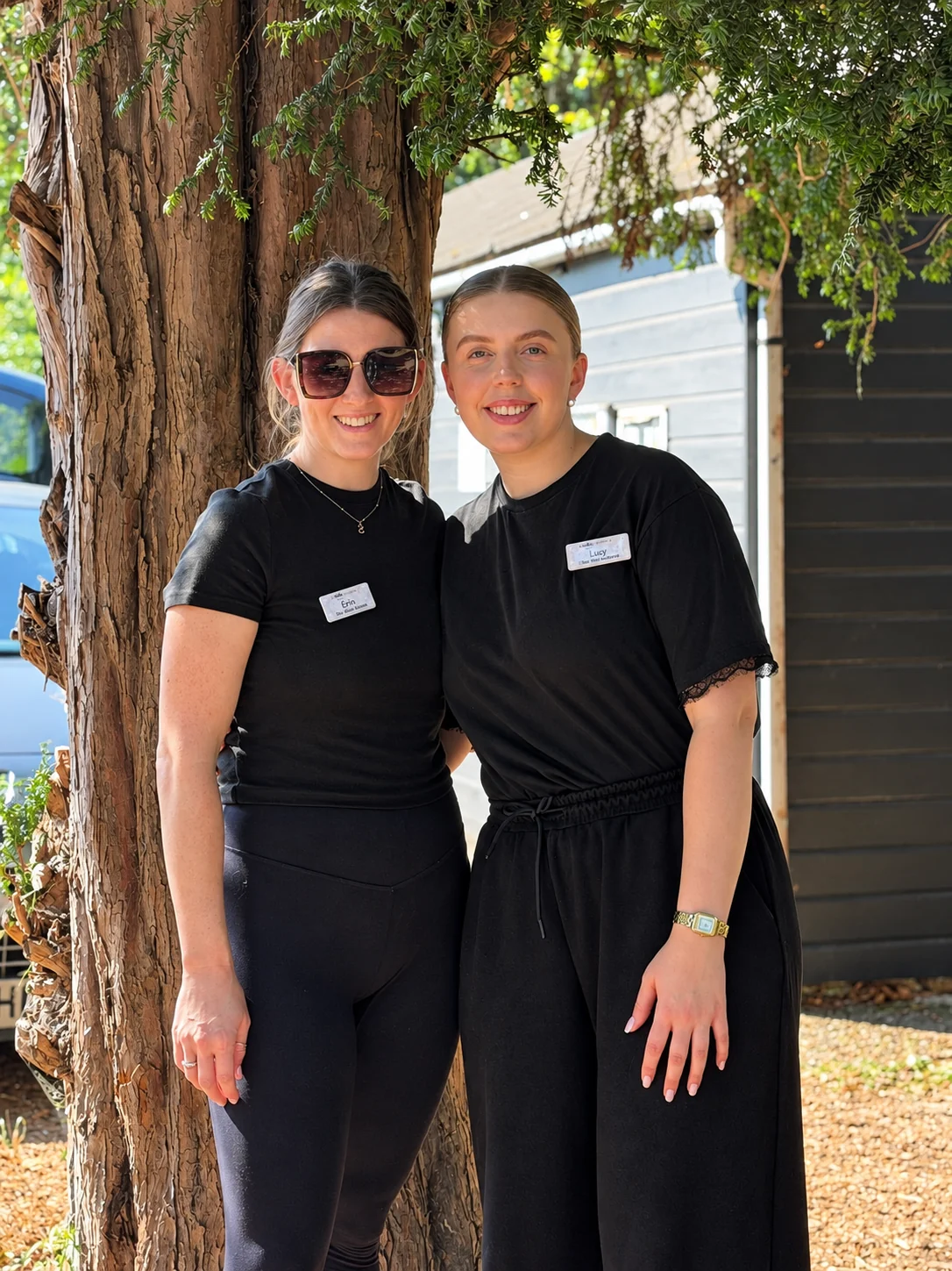 Two team members in black uniforms standing together beside a tree