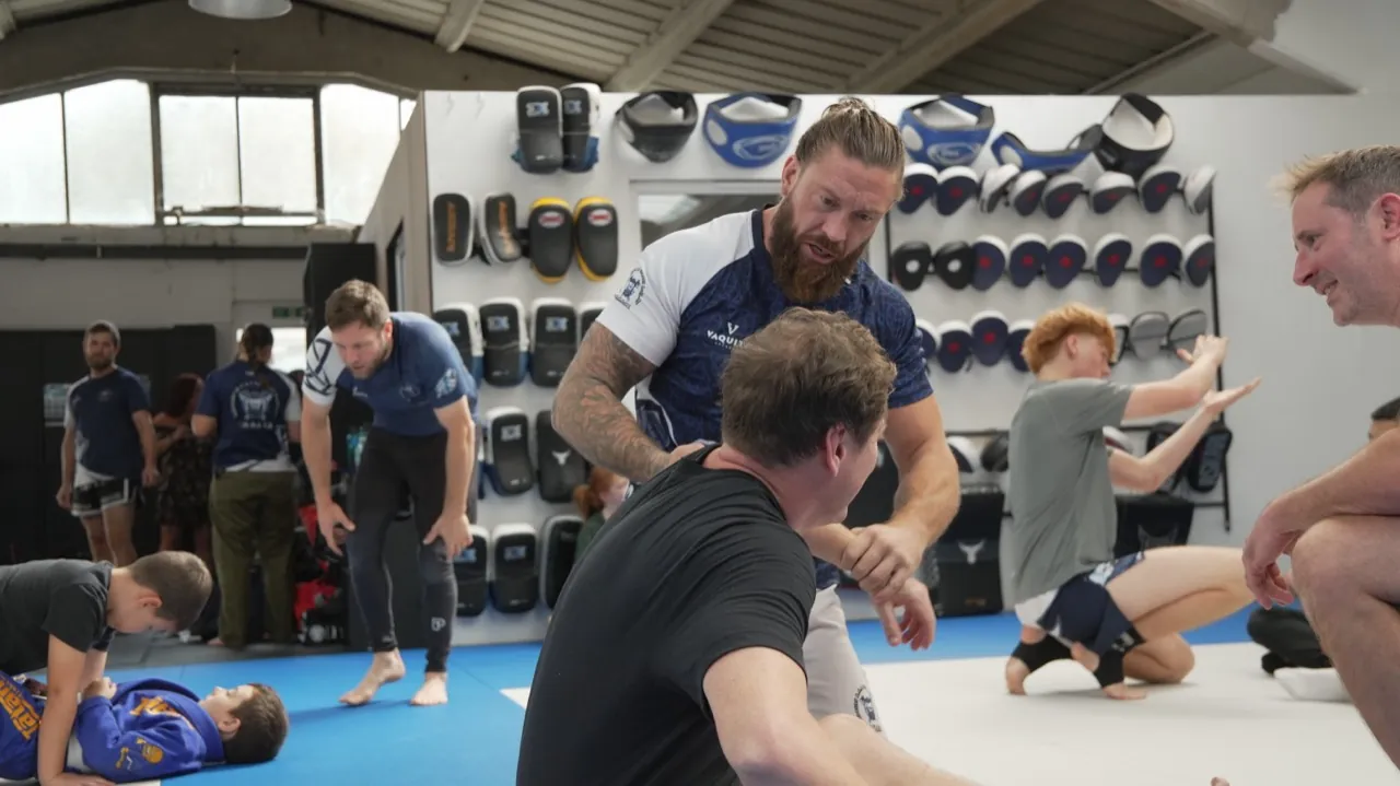 Coaches and students training together on the mats, pads lining the wall behind them