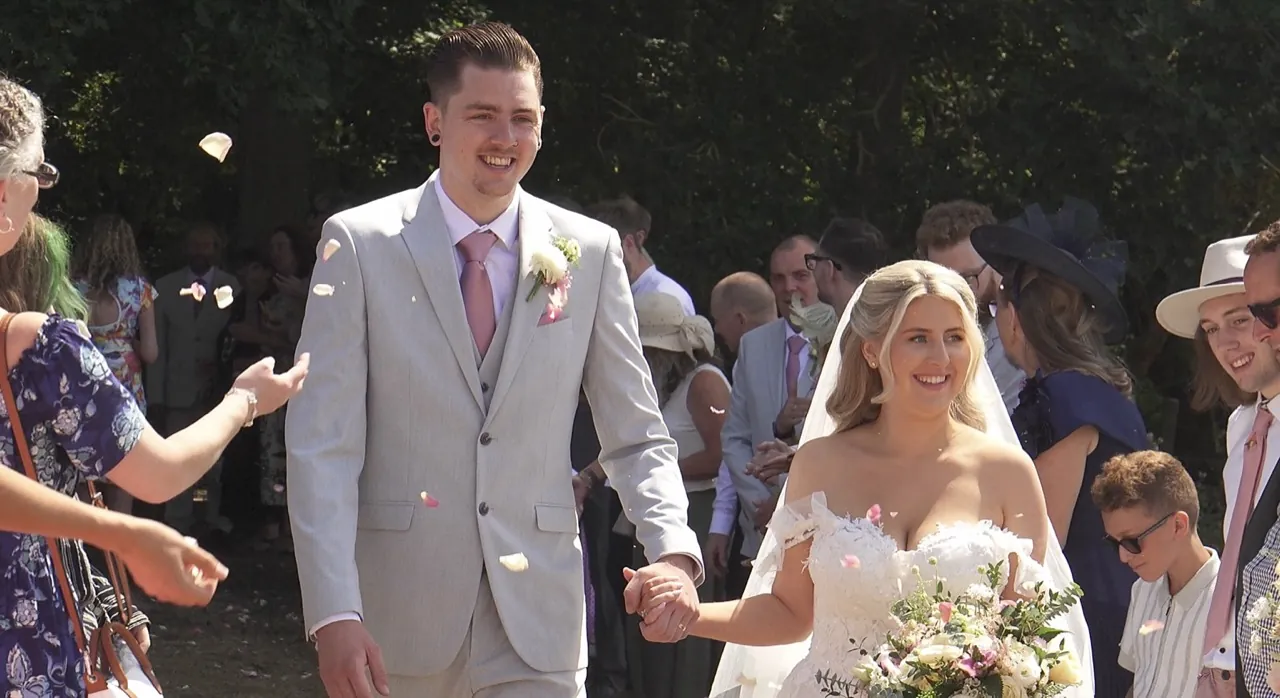 Newlyweds walking hand in hand through confetti, surrounded by their guests